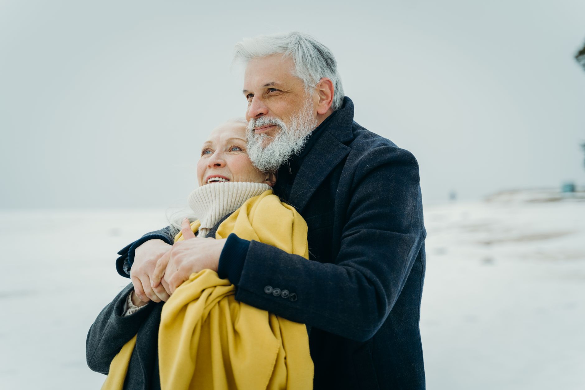 Elderly couple embracing warmly on a snowy beach. Love and connection in winter.