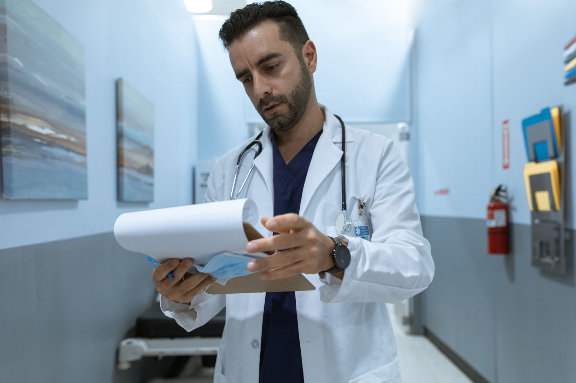 Male doctor in hospital hallway reviewing medical charts, focused and dedicated.