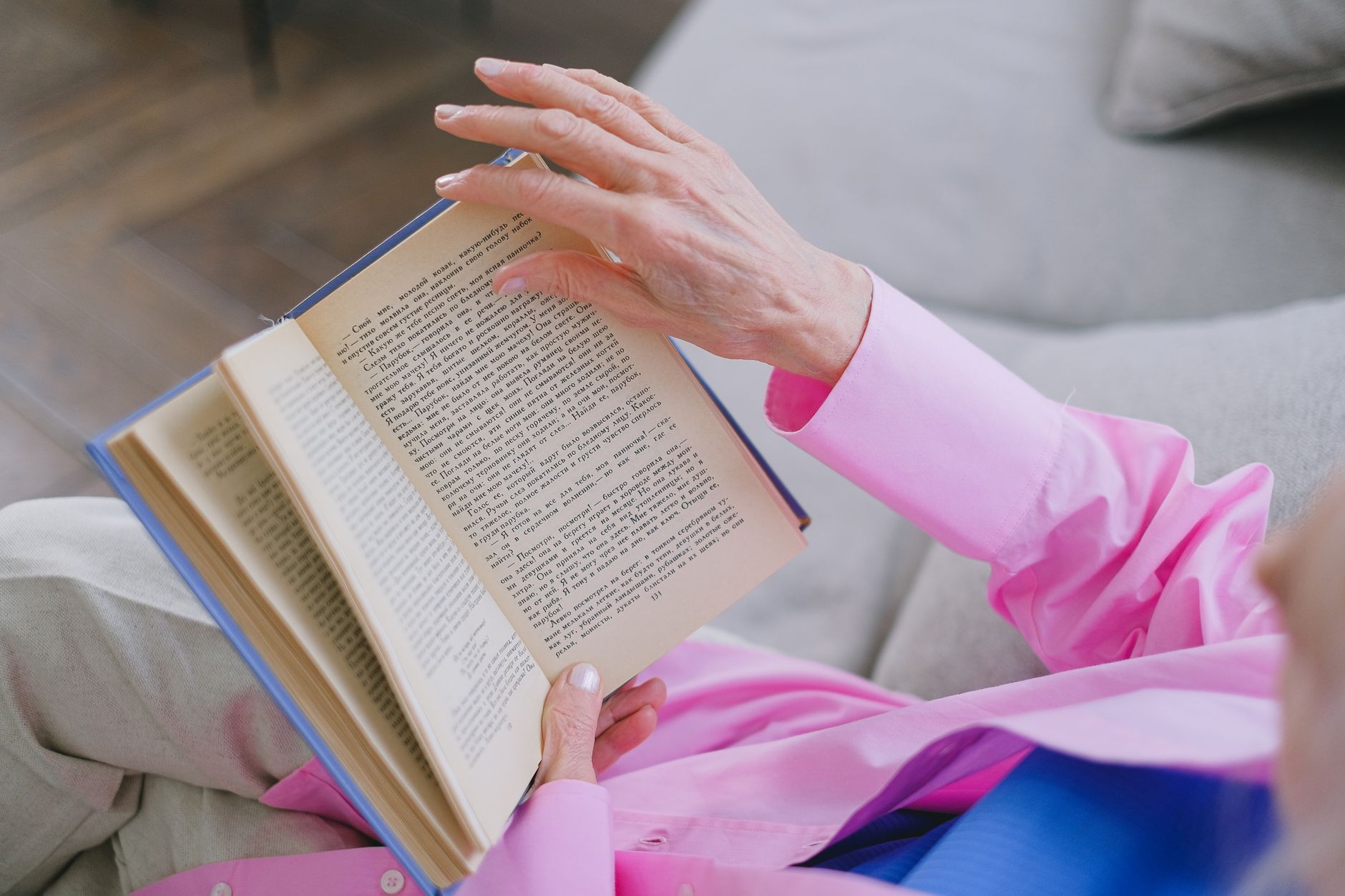 Senior woman in pink shirt reading book, relaxed on sofa at home.