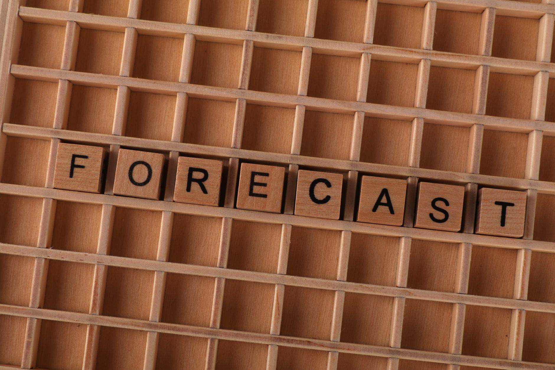 Scrabble-like wooden blocks spelling the word 'forecast' on a wooden grid surface.