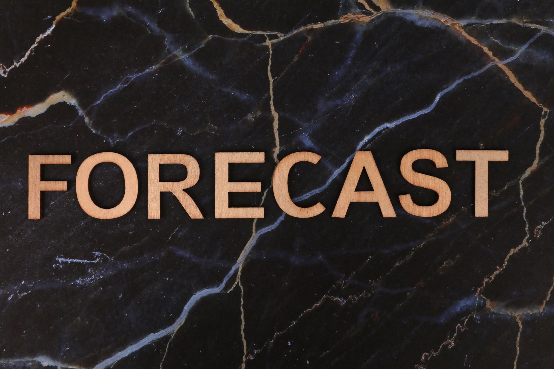 The word 'FORECAST' in wooden letters on a dark marble background.