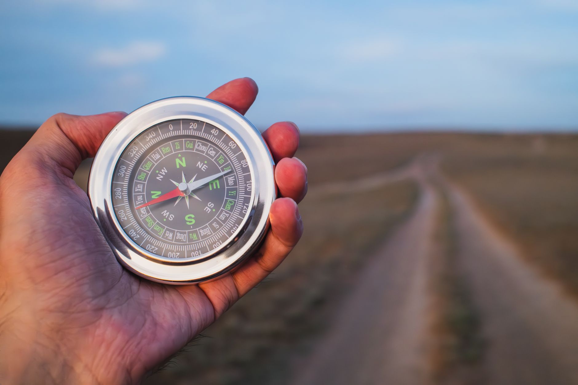 Close-up of a hand holding a compass against a rural path, symbolizing exploration.
