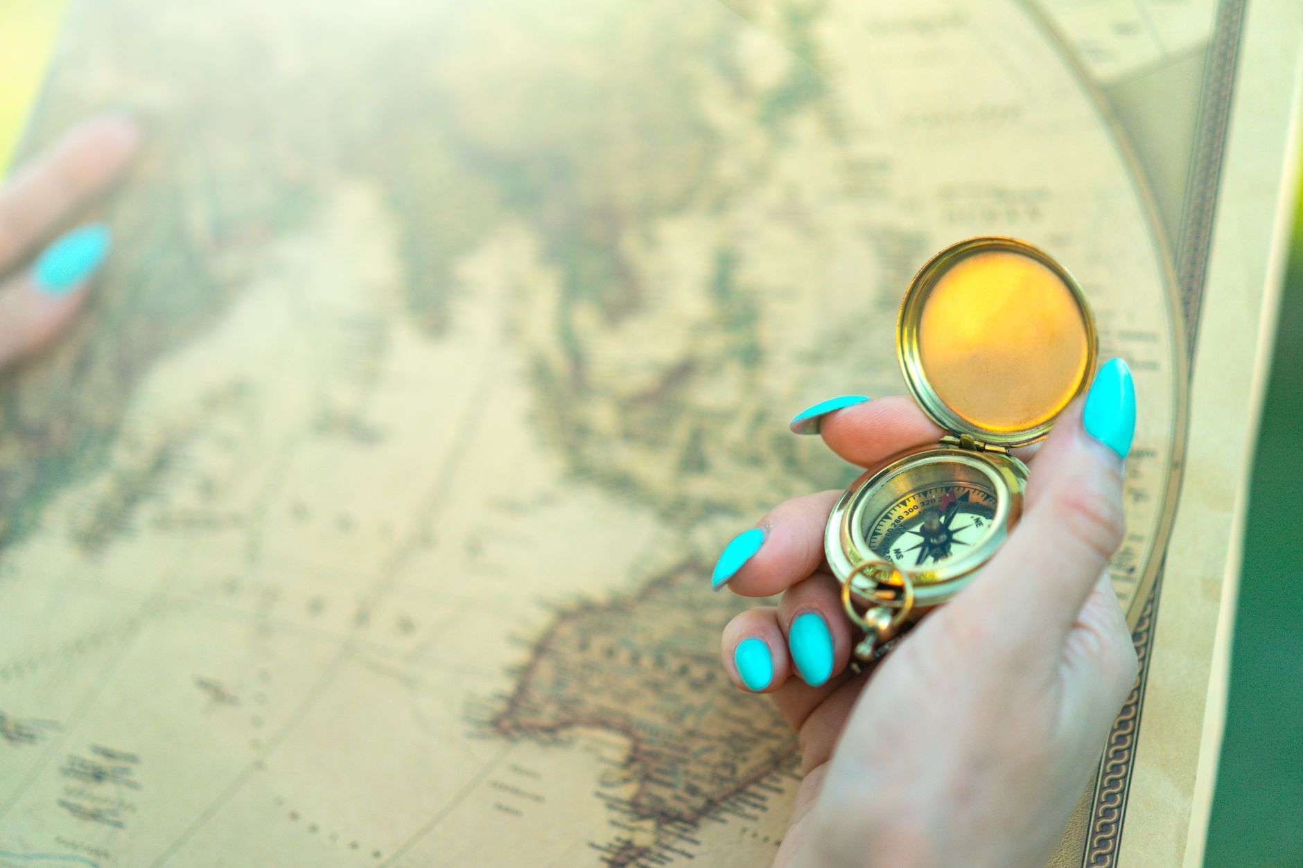 Close-up of a hand holding a vintage compass over an ancient map, symbolizing exploration and travel.