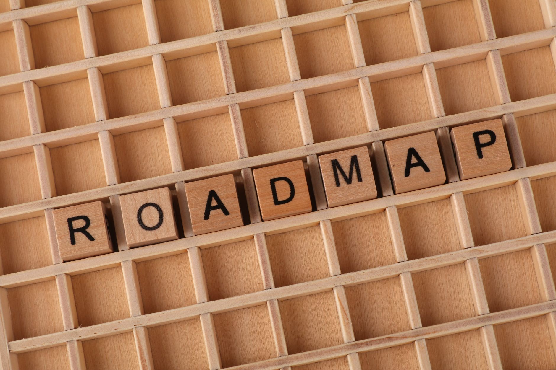Wooden letter blocks spelling ROADMAP on a square grid layout, top view.