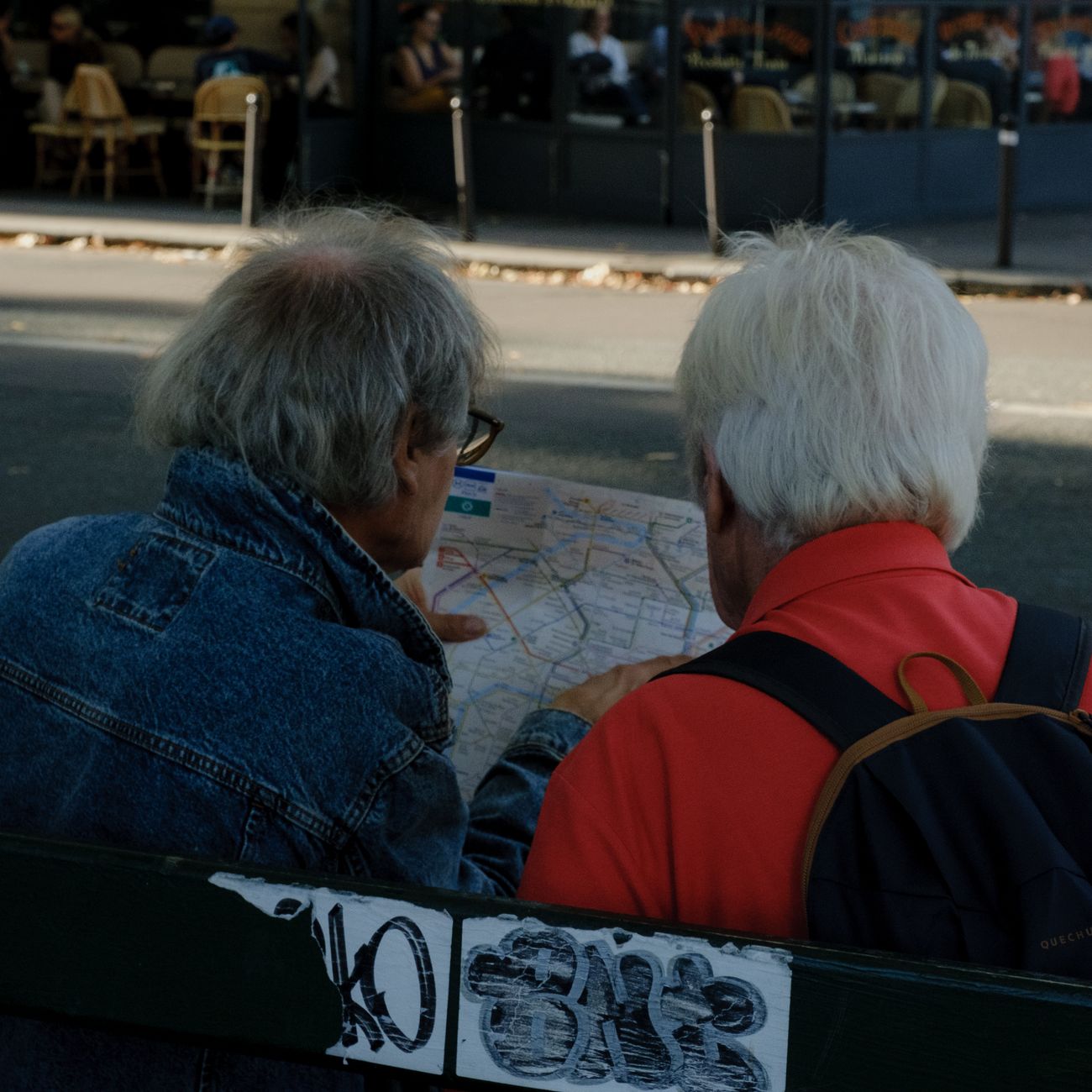 Two senior adults reading a map while sitting on a bench in an urban setting.