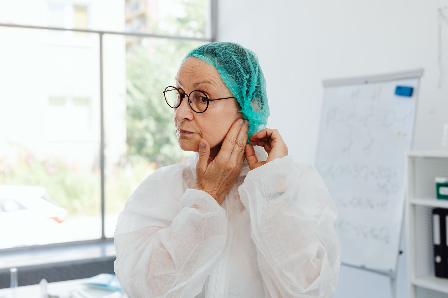 Elderly woman adjusting protective gear in a laboratory setting, ensuring safety measures.