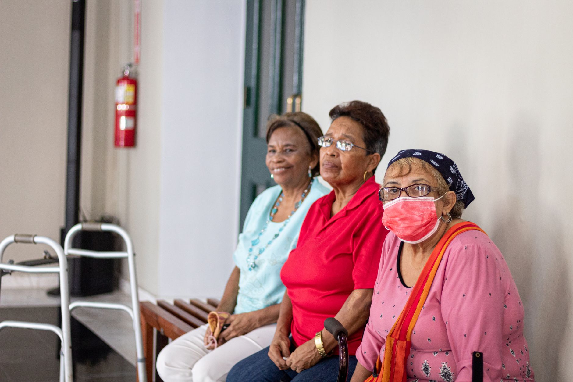 Three senior women sitting indoors, one wearing a face mask, in a safe environment.
