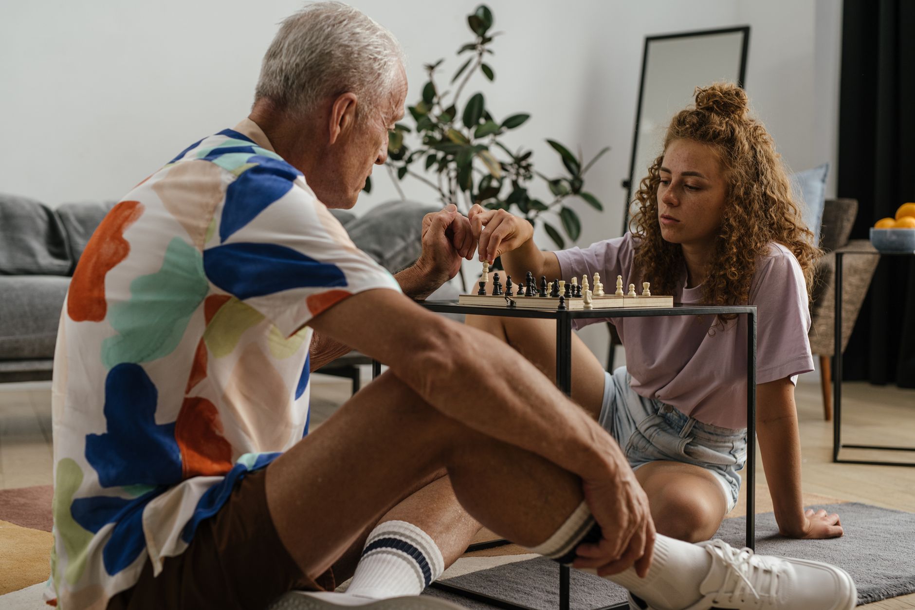 A grandfather and granddaughter spend quality time playing chess indoors, fostering family bonding.