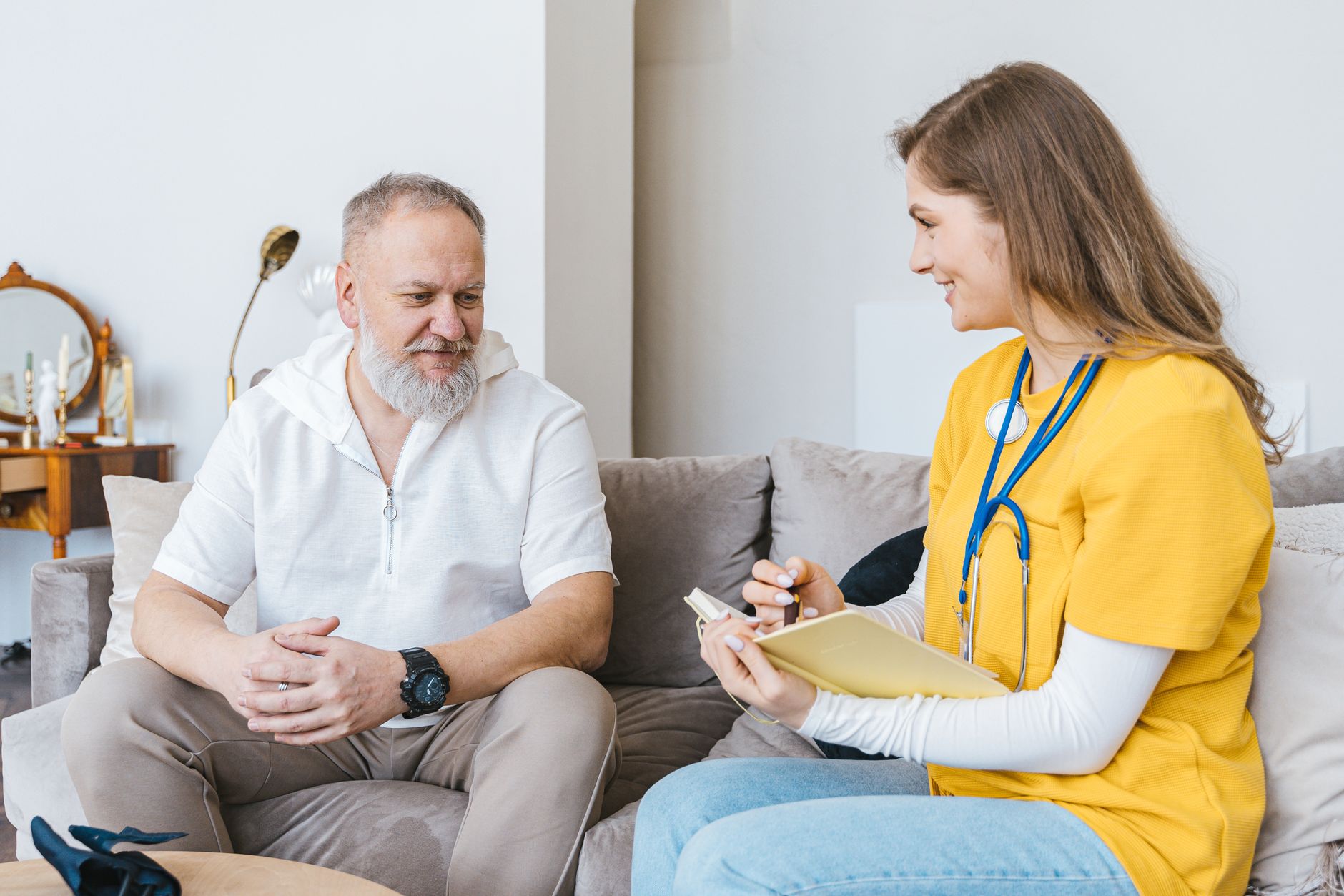 A healthcare professional smiles while consulting with an elderly man in a cozy indoor setting.