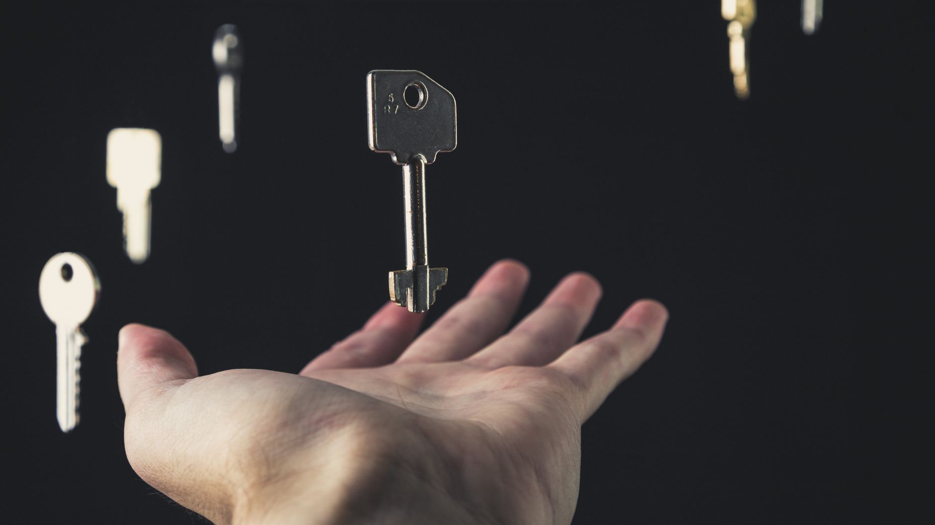 A mysterious scene of keys floating above an open hand against a dark background.